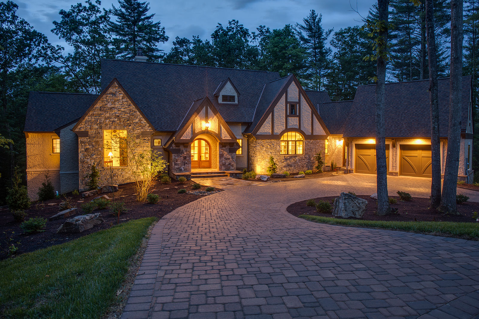 Stone and stucco custom-built Tudor mansion on a wooded lot at twilight.